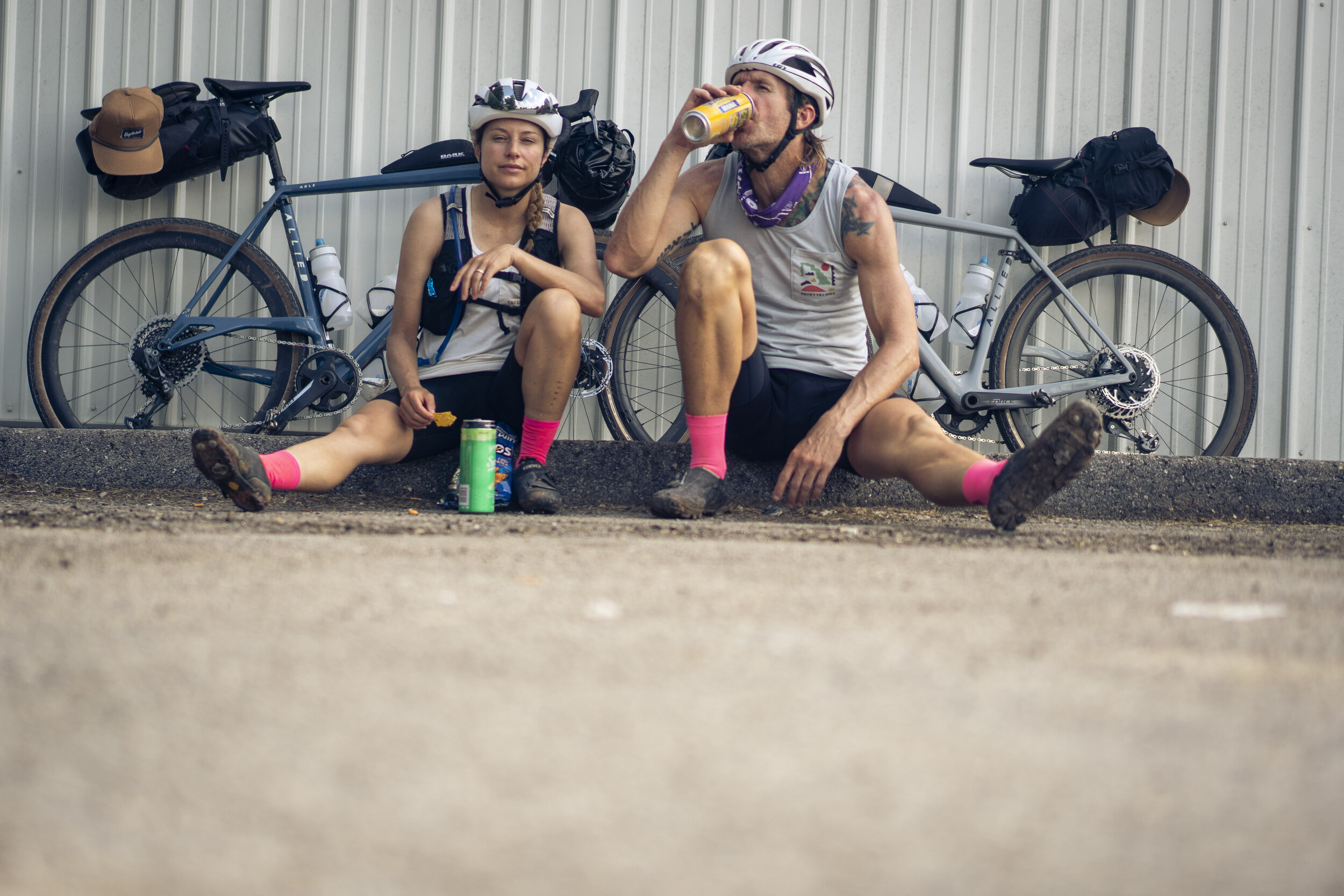 Male and female cyclists sitting on the ground in front of their bikes eating snacks.