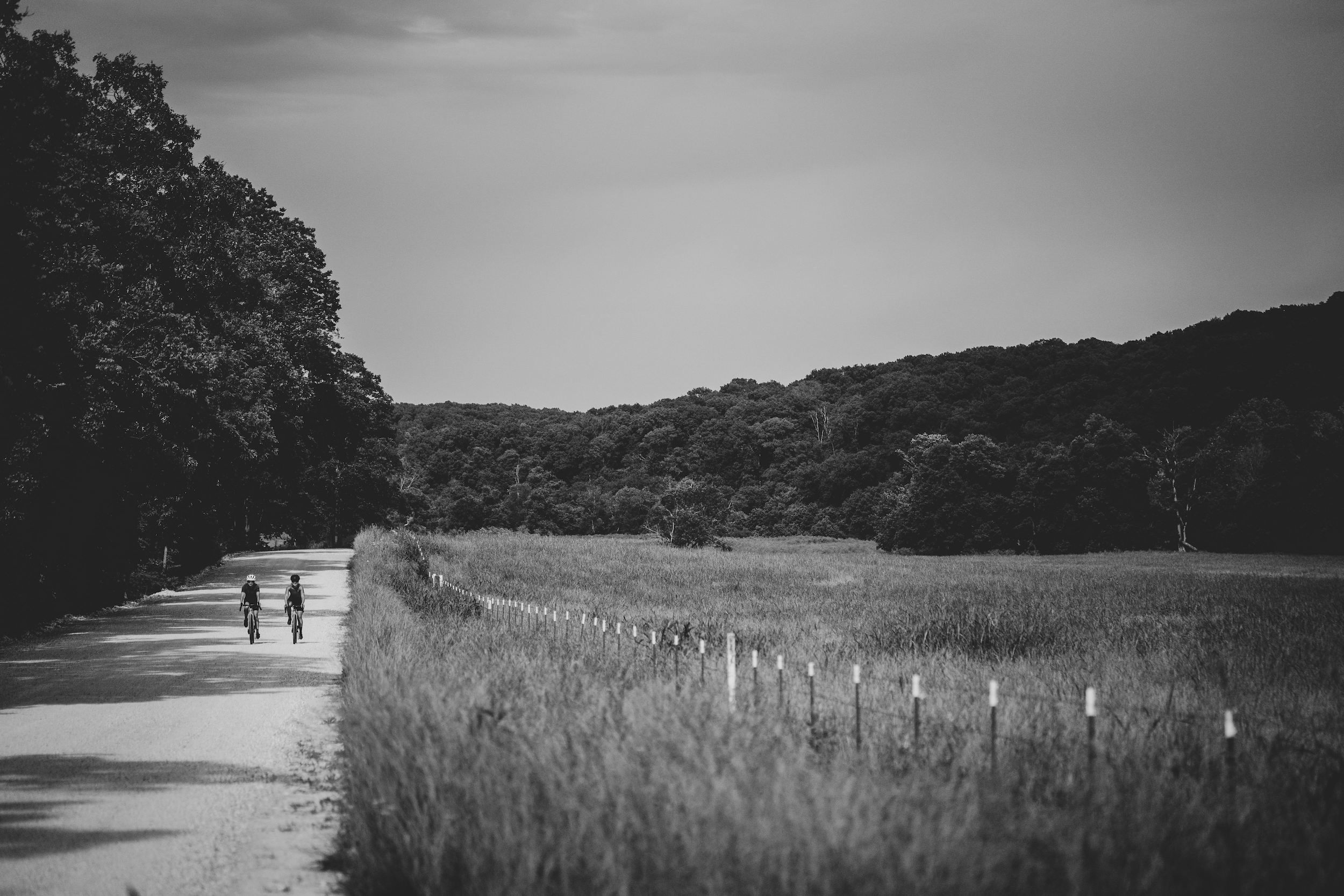 Two people ride their bike down a gravel road in the black and white photo.