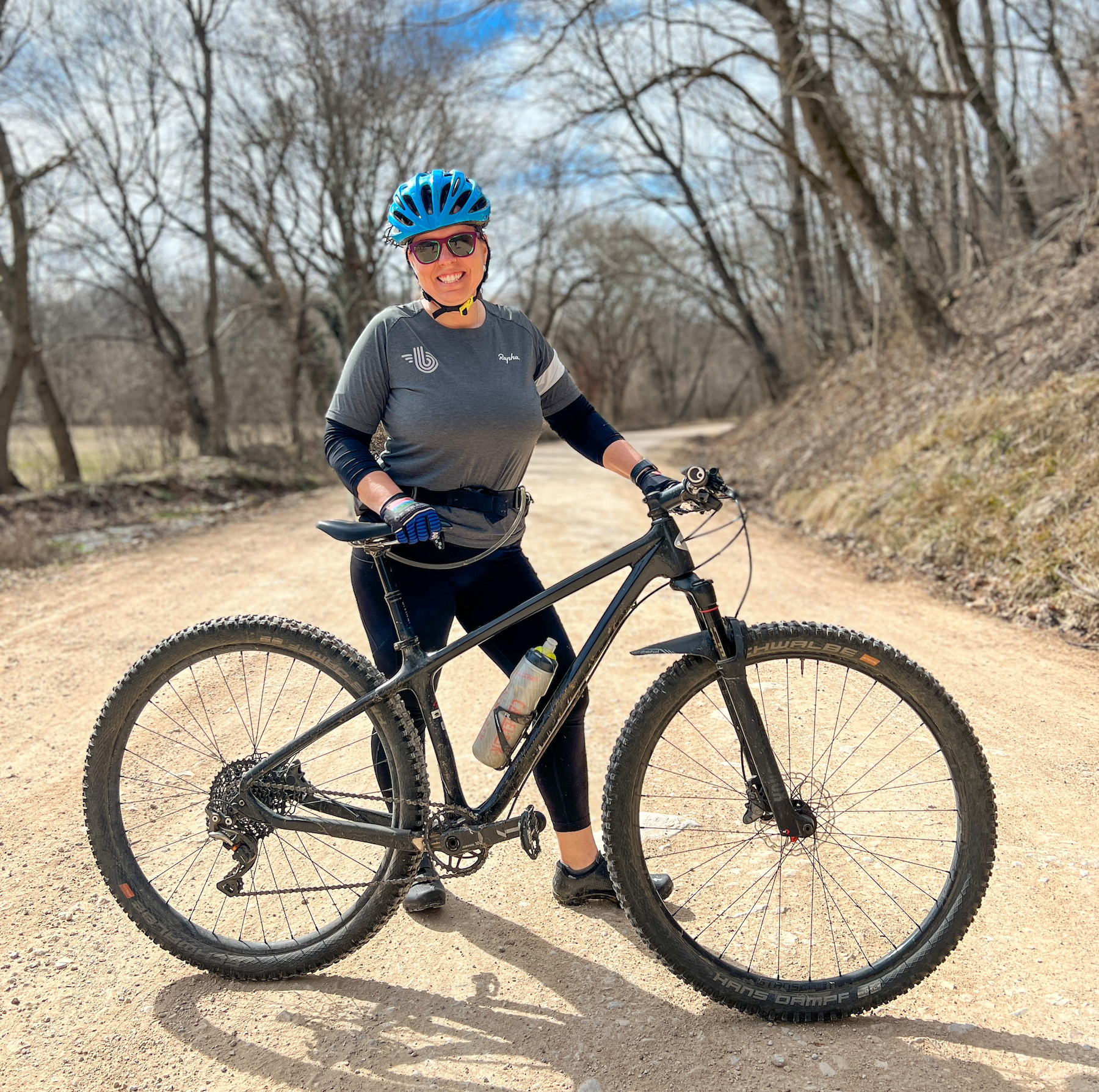 A female rider poses with her mountain bike on a gravel road.