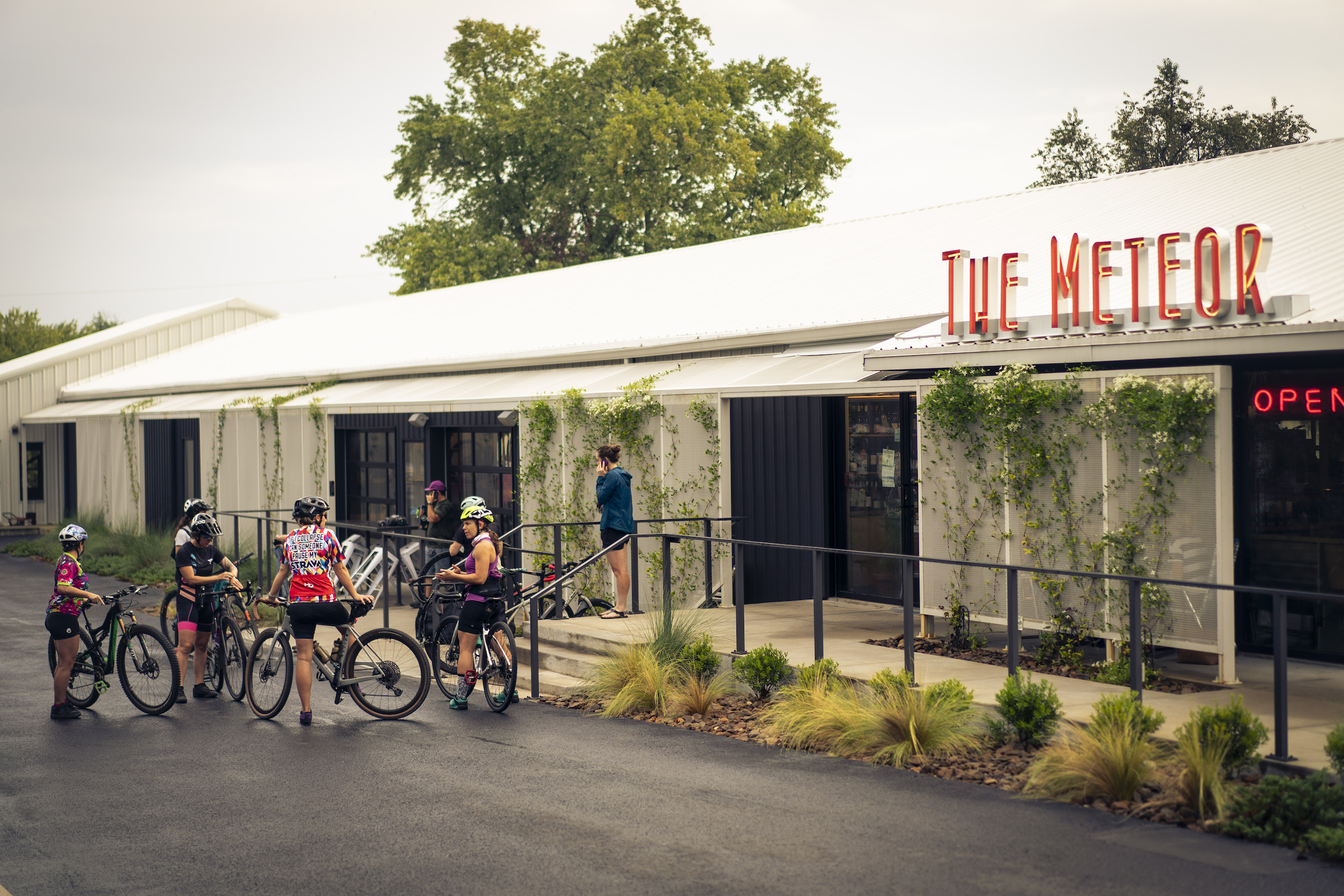 5 ladies stand outside Meteor Cafe with their bikes getting ready to go for a ride