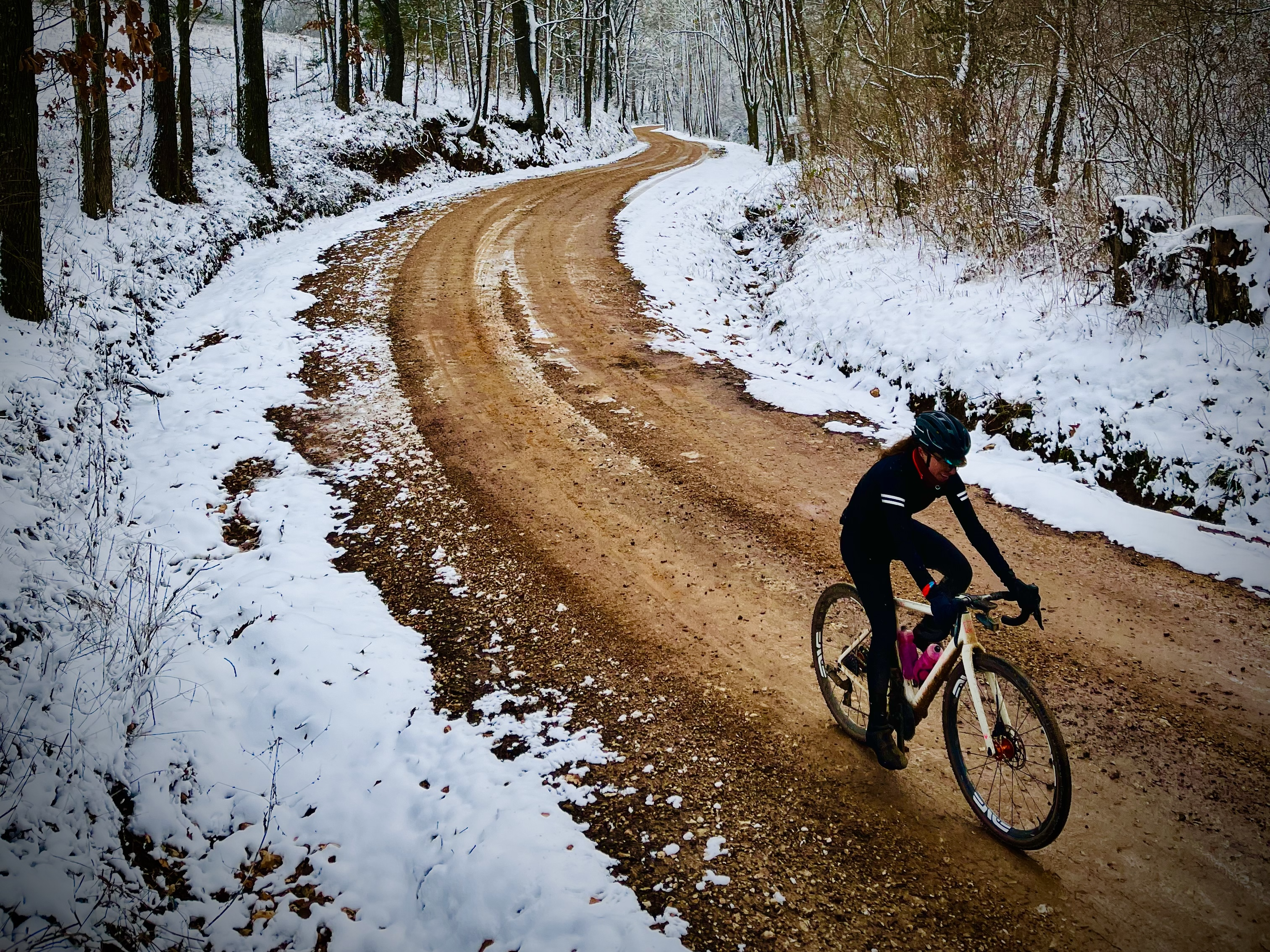 A person rides a gravel road with snow on the side of the road.