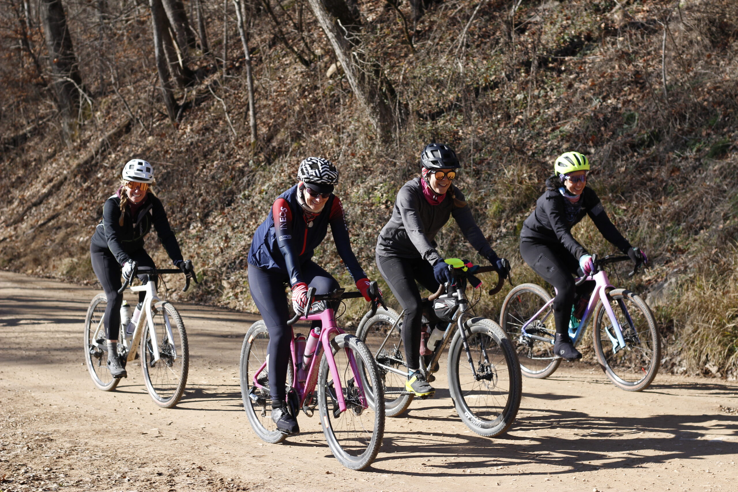 A group of four ladies smile as they ride past on their gravel bikes.